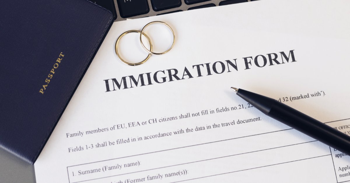 An immigration form with a passport, two rings, a pen, and a keyboard on a desk with blank application lines.
