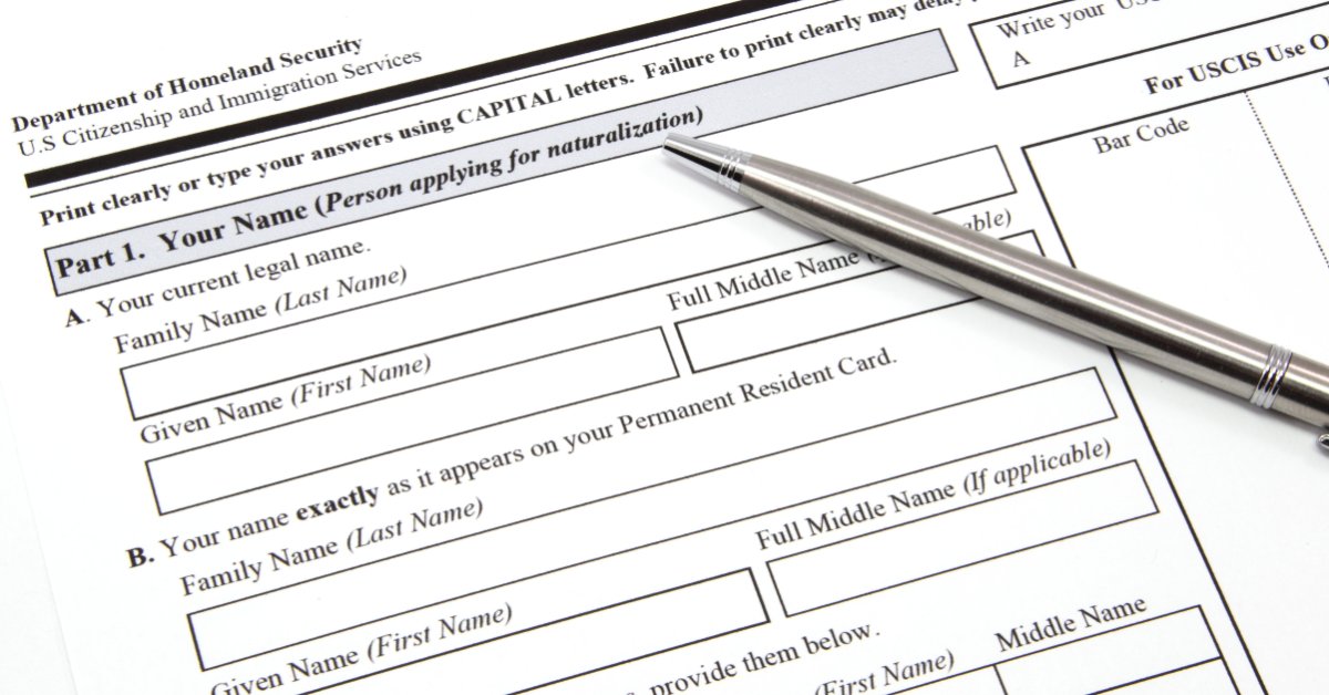 A citizenship application form with blank name fields and a silver pen resting across the upper section.