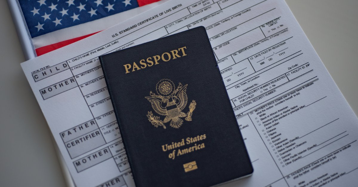 A United States passport lying on a live birth certificate form with an American flag in the background.