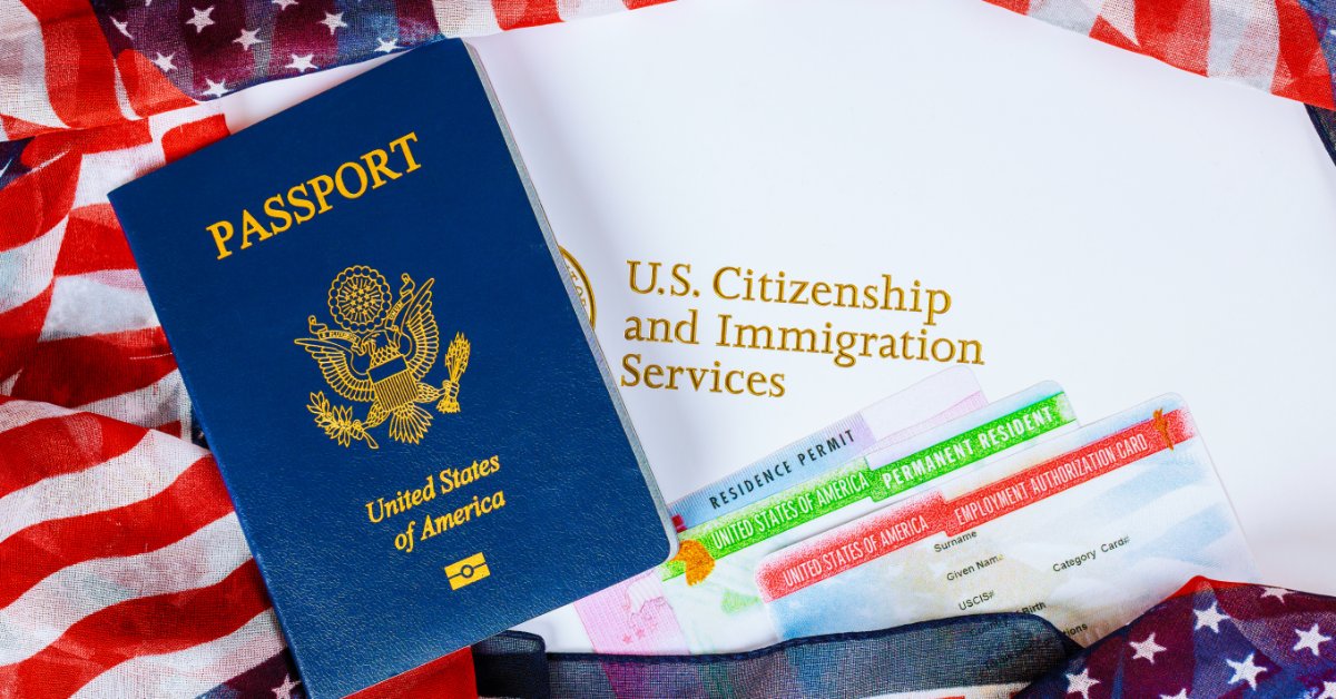 A blue U.S. passport, immigration papers, permit cards, and an American flag lie arranged on a tabletop.