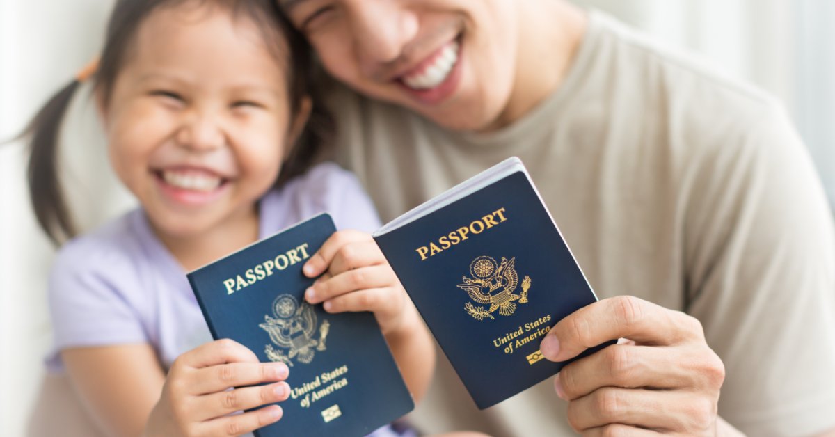 A smiling adult and child holding blue United States passports while sitting closely together indoors.