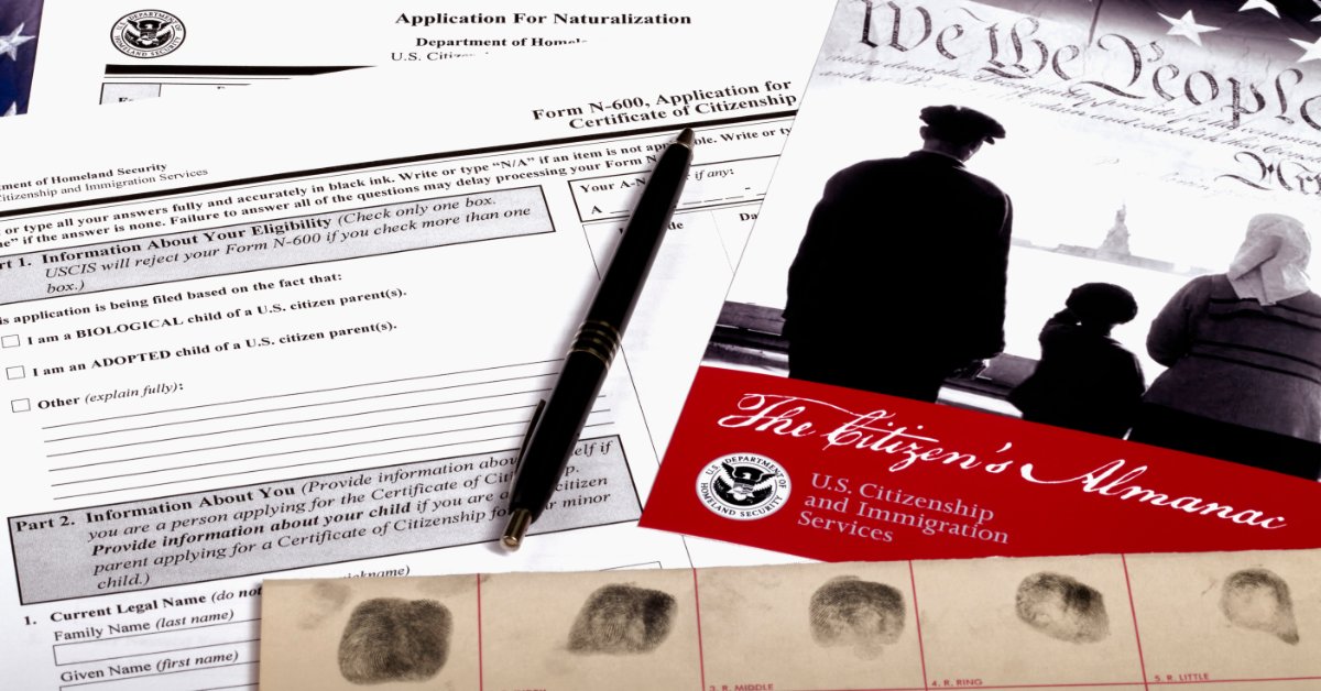 Naturalization forms, a fingerprint card, a black pen, and U.S. government documents arranged on top of the U.S. flag.