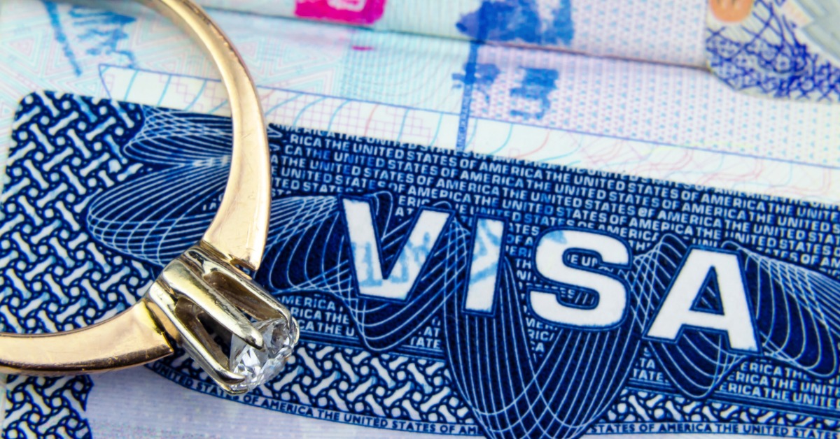 A gold engagement ring resting on a blue visa page in a passport with colorful stamps in the background.