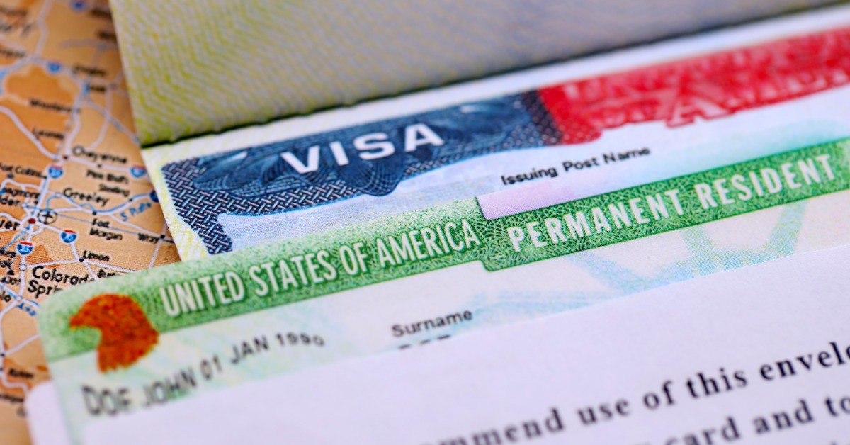 A green U.S. permanent resident card overlapping a printed visa document on a road map of the United States.