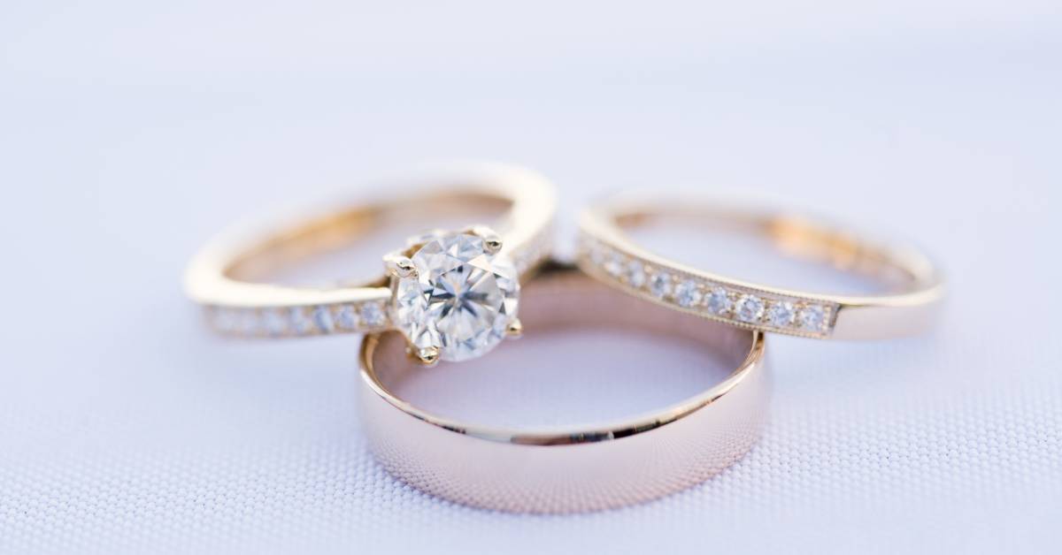 An engagement ring and two wedding rings. All three rings are gold; however, only two have inlaid diamonds.