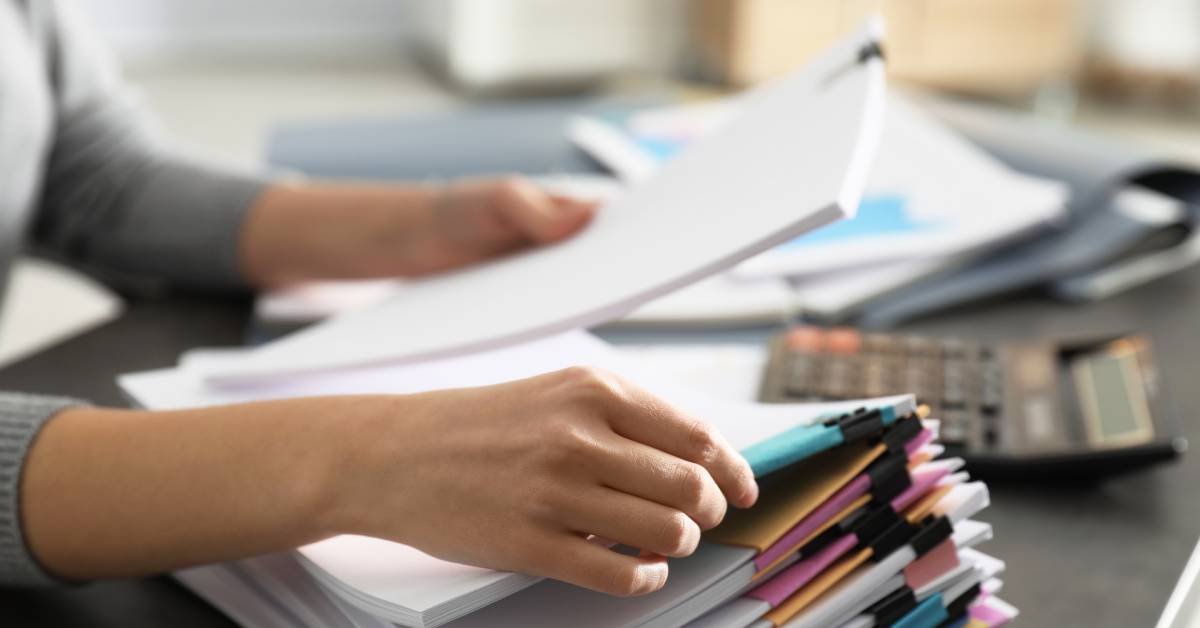 An individual is looking through stacks of paperwork. The papers are divided with paper clips and color coded.