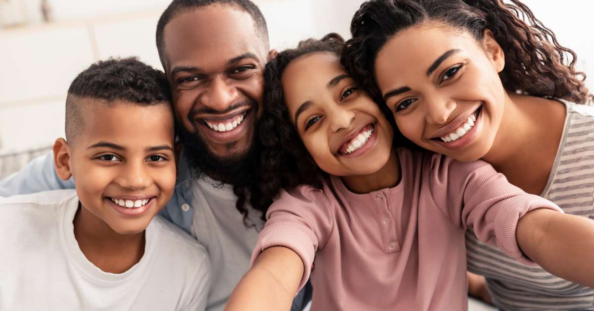 A mother, father, son, and daughter sitting close to each other and smiling while taking a family selfie.