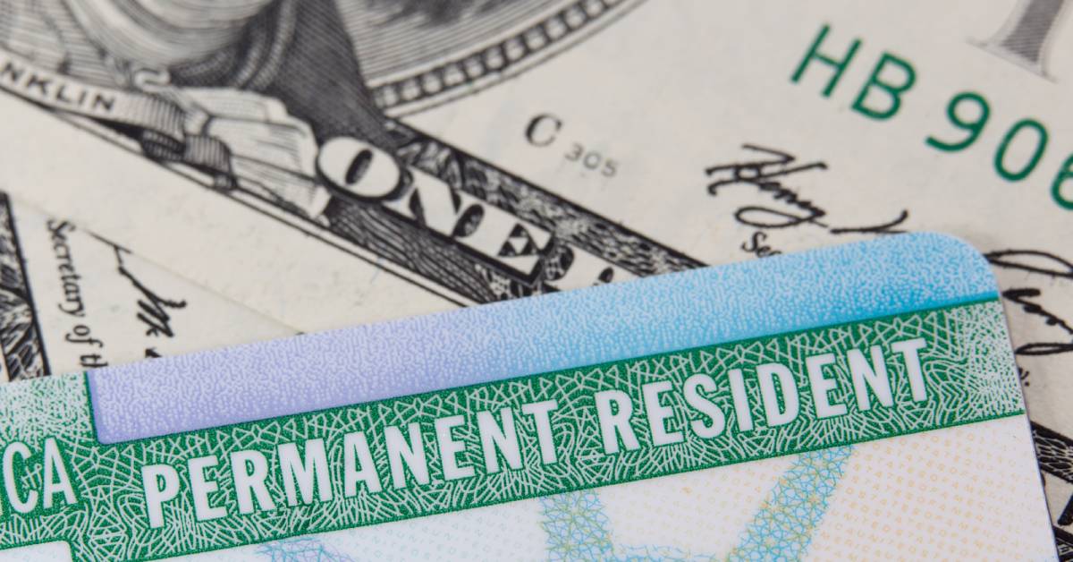 A close-up of a permanent resident card, also known as a green card. There is US currency behind the card.