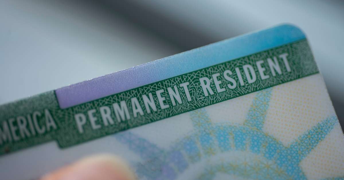 A close-up of a person holding a permanent resident card. The card features the Statue of Liberty.