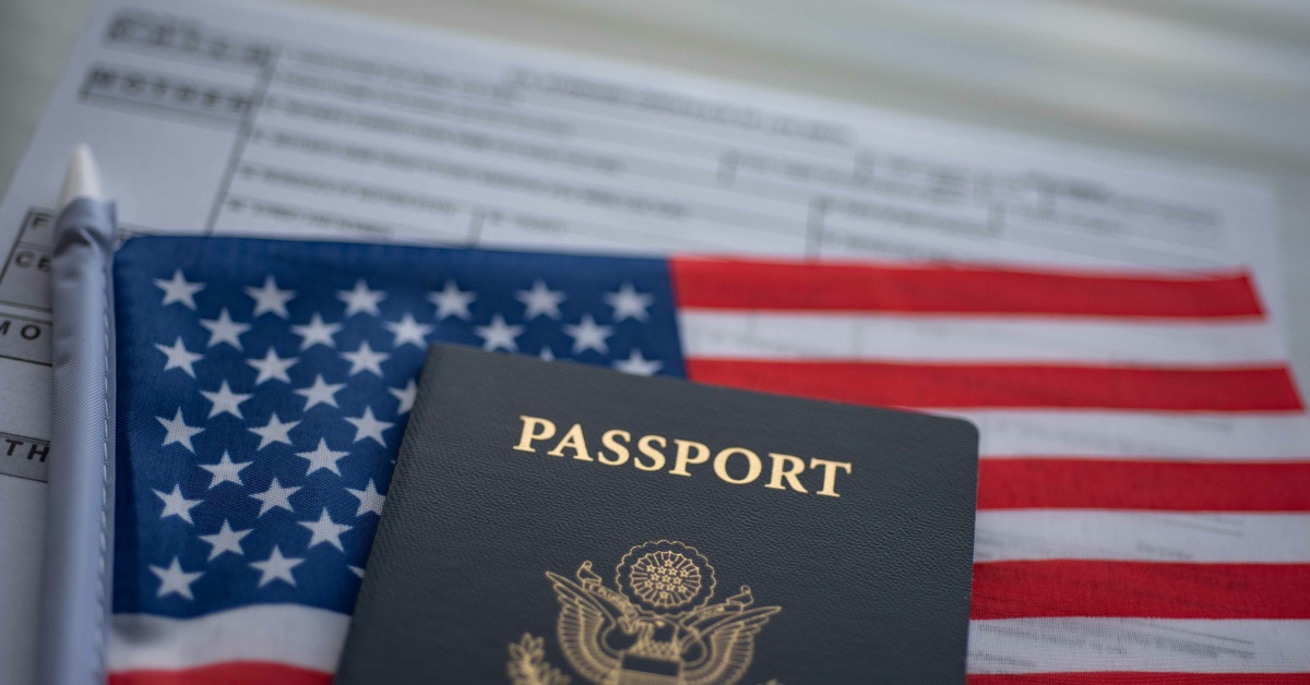 A close-up of a United States passport placed on top of an American flag. There is a blurred document under the flag.