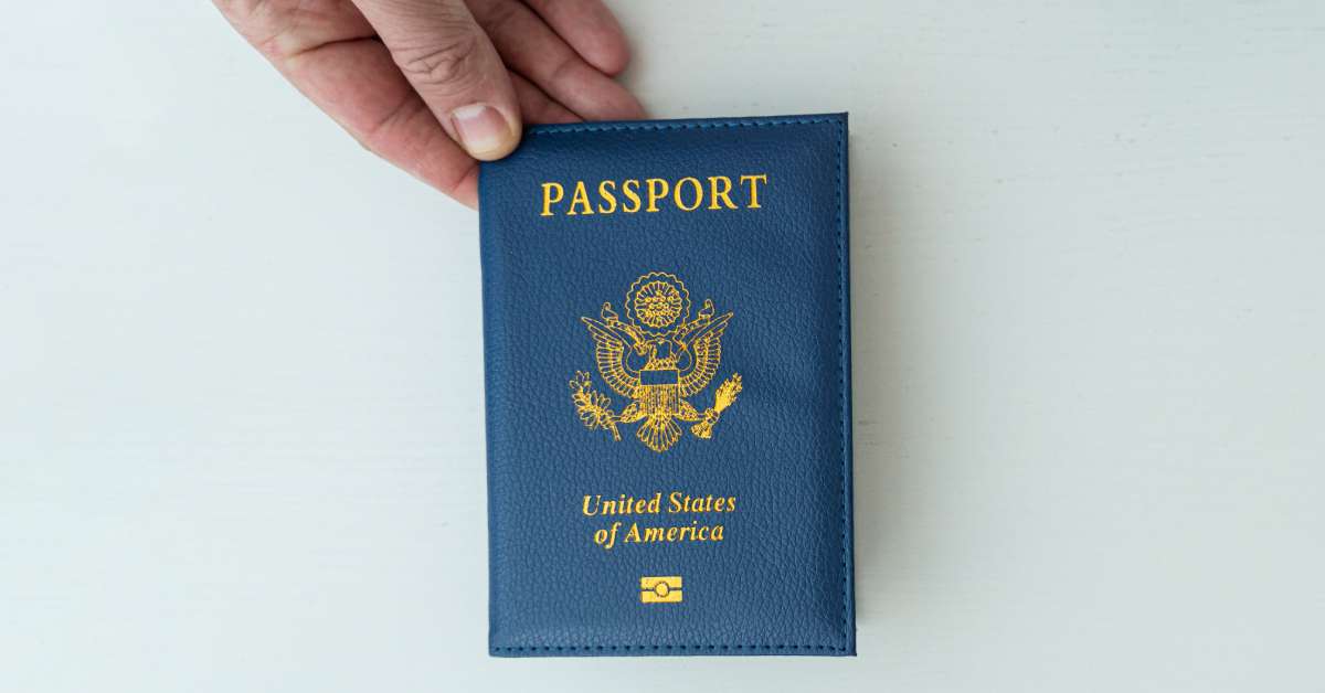 A close-up of a person's hand holding a blue United States passport book. The passport has gold foil text on the front.