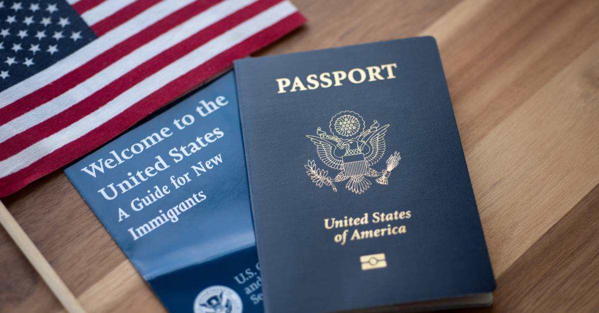 An American flag, a guide for new immigrants, and a US passport arranged next to each other on a wooden surface.