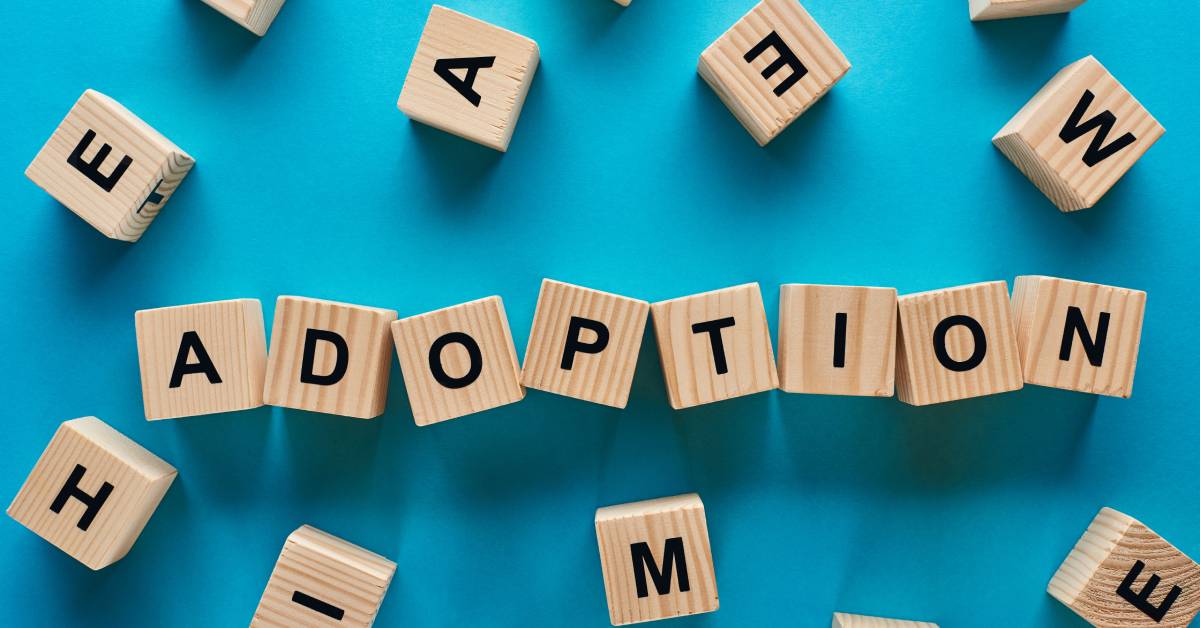 An overhead view of the word "adoption" spelled out with wooden cubes on a blue background. Each cube has one black letter.