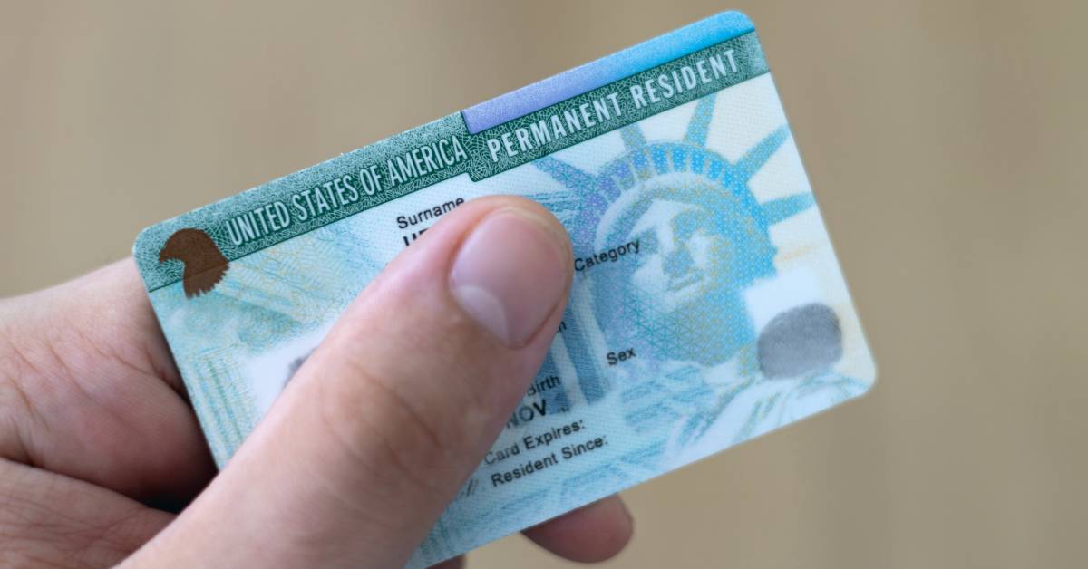 A close-up of someone holding a United States of America Permanent Resident Card against a beige background.