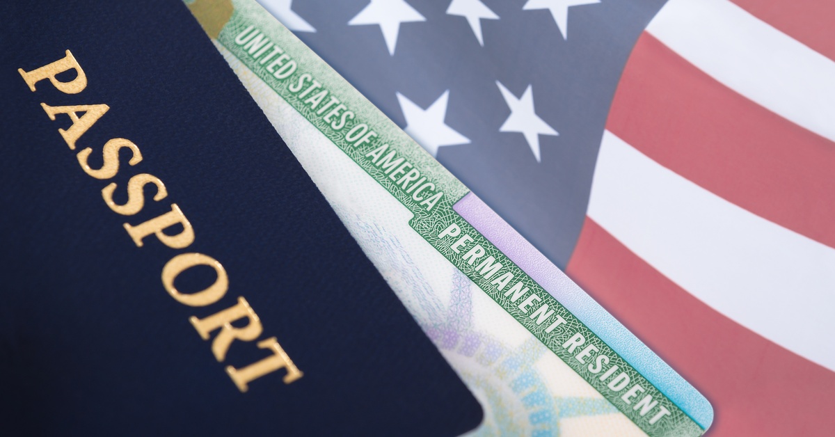 A blue passport with a United States Permanent Resident card behind it against an American Flag background.