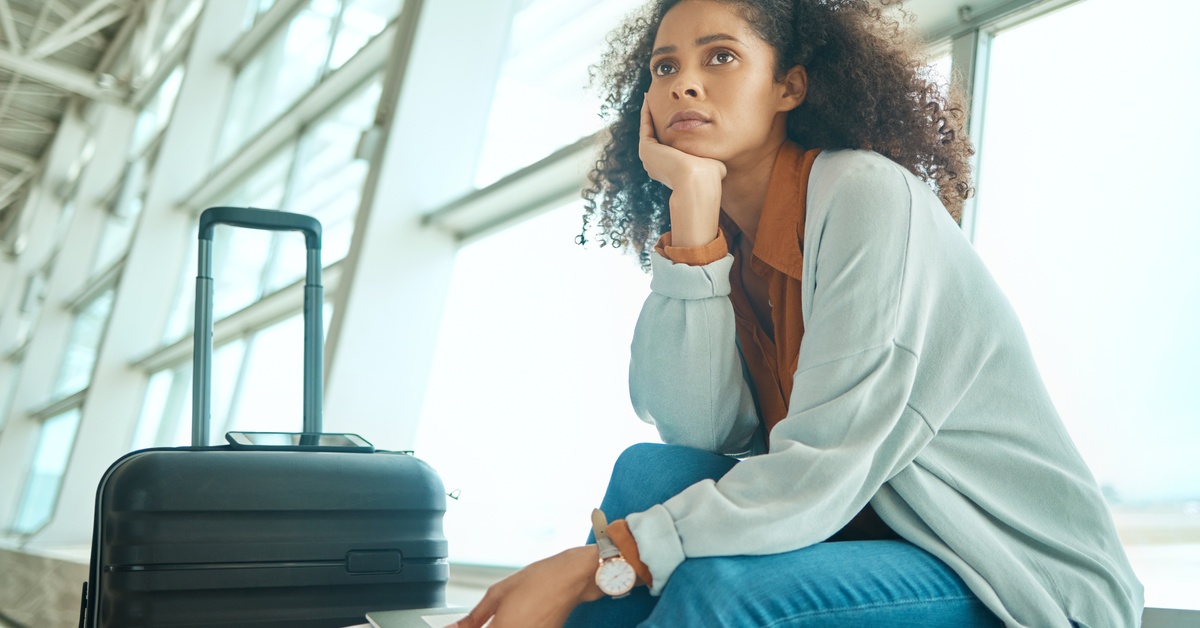 A young woman looks anxious as she sits by the airport window holding her green card next to a black luggage.