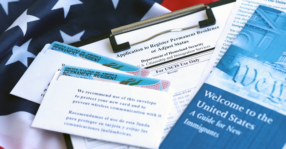 A brochure that says "Welcome to United States" sits next to two Green Cards, and an application for Adjustment of Status.