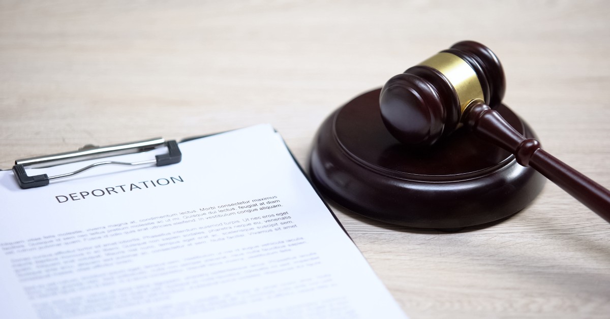 A clipboard with deportation documents sit on top of a wooden table while sitting next to a wooden gavel.