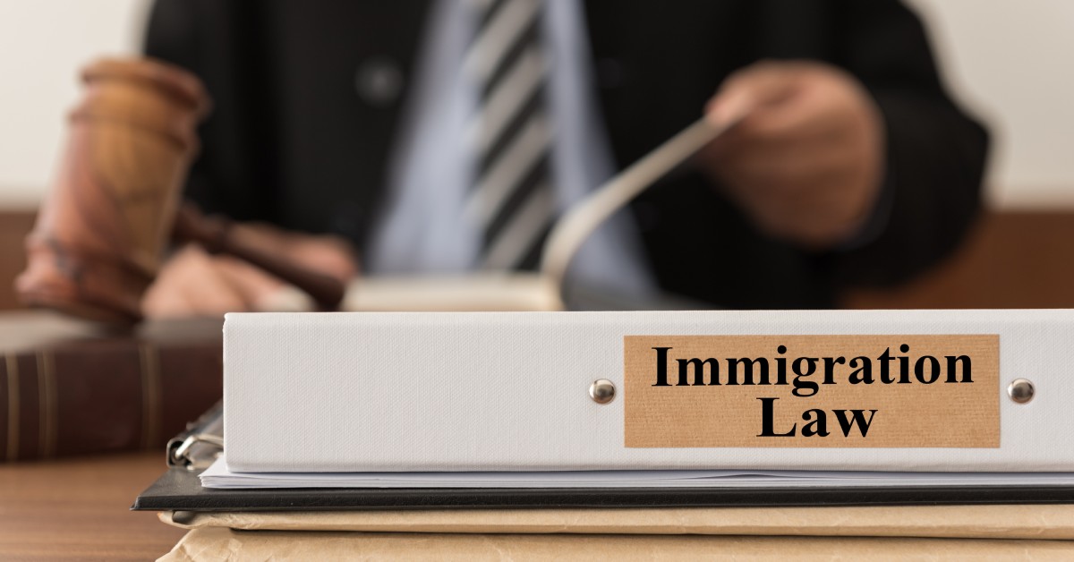 A white binder with the words immigration law on it sits on top of a stack of documents, near a wooden gavel.