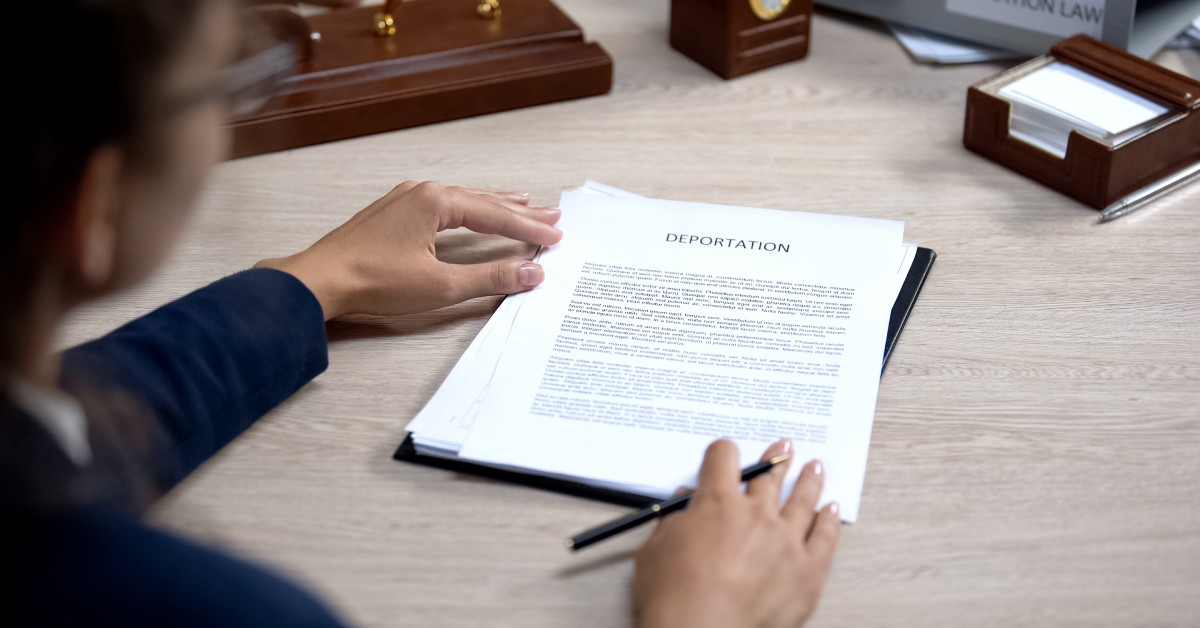 A person wearing eyeglasses and a blue suit holds a pen in her hand while looking at deportation documents.