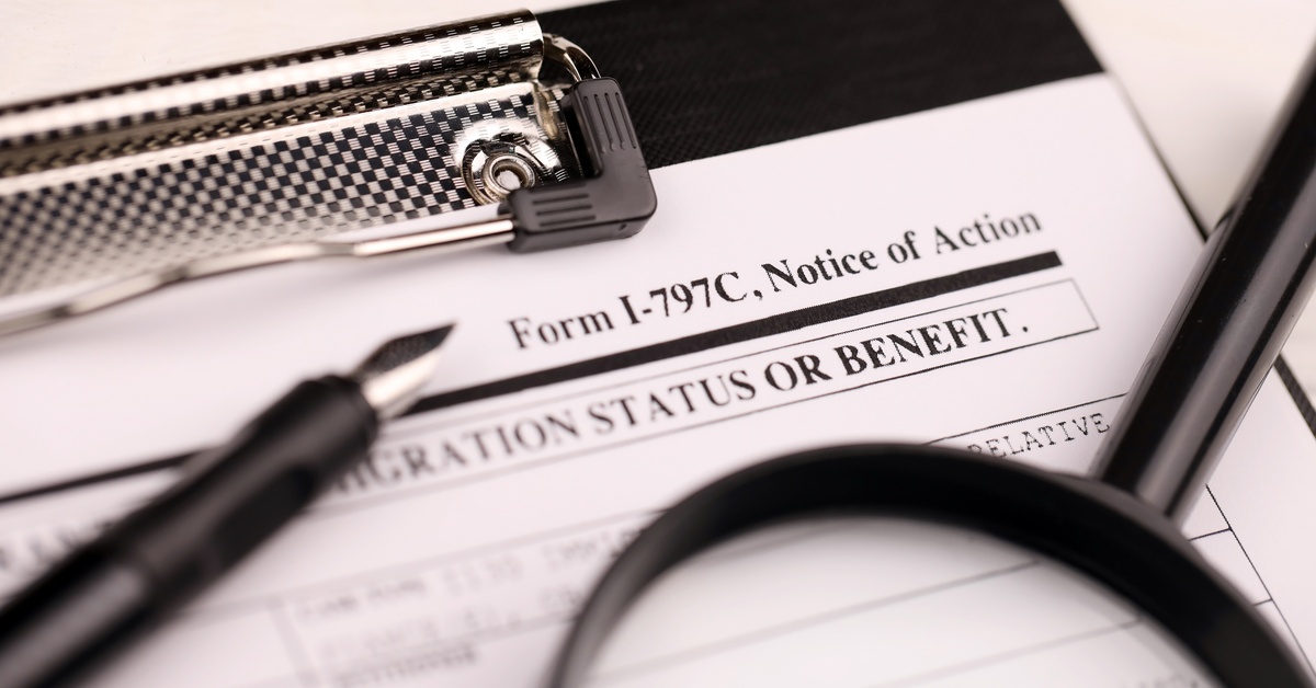 A black clipboard with a document called Form I-797C sits next to a black pen and a magnifying glass on the table.