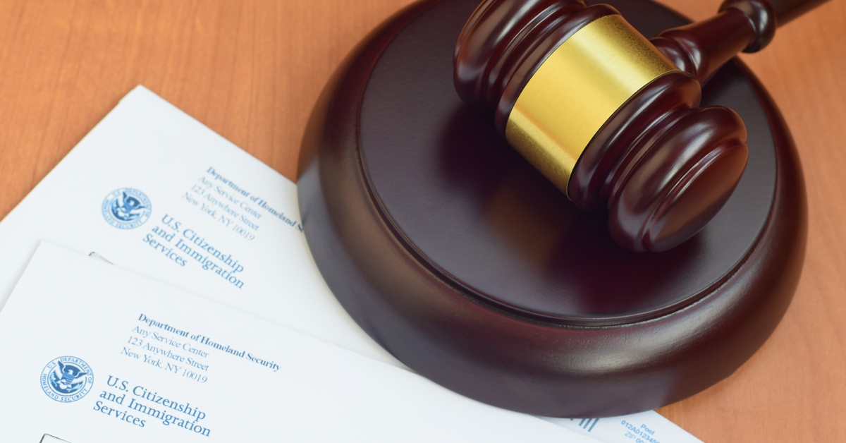 A brown, wooden gavel sits on top of multiple U.S. Citizenship and Immigration documents sitting on a table.
