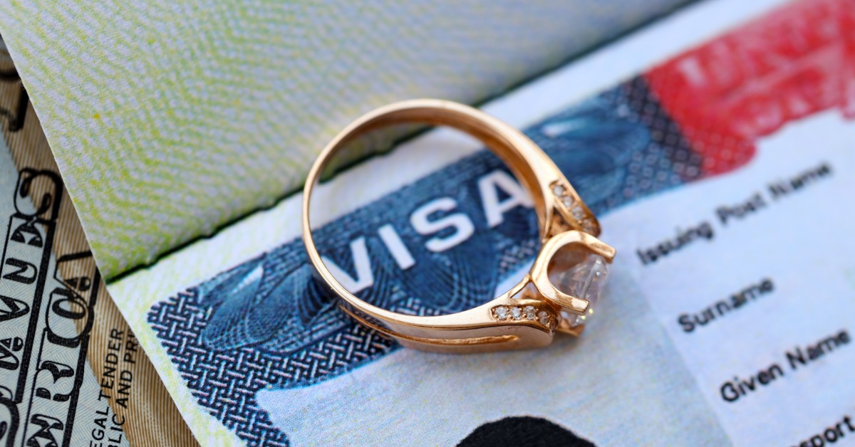 The light reflects off of a rose-gold diamond ring resting on top of an open United States Visa document.