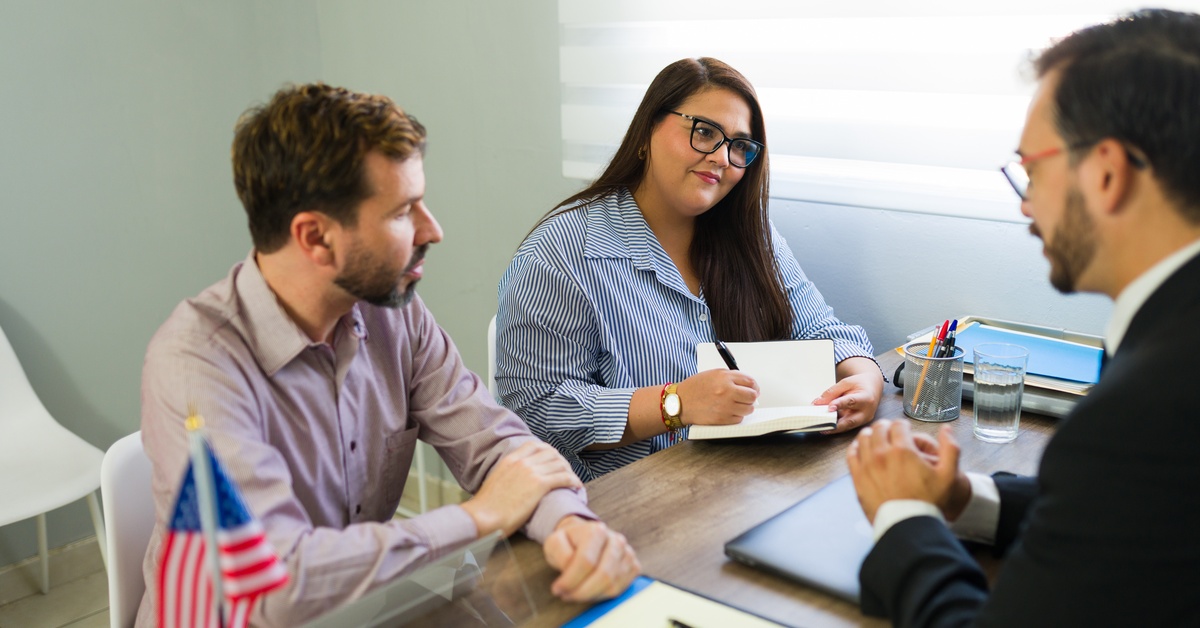 A man and a woman wearing eyeglasses takes notes on a notebook while listening to a U.S. immigration lawyer.