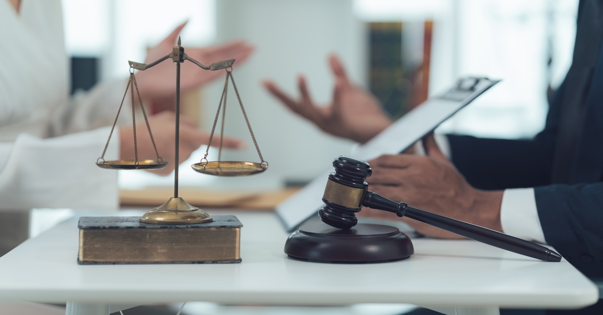 A client is seeking legal counsel. In front of them is a gold scale of justice sitting on top of a book, and a gavel.
