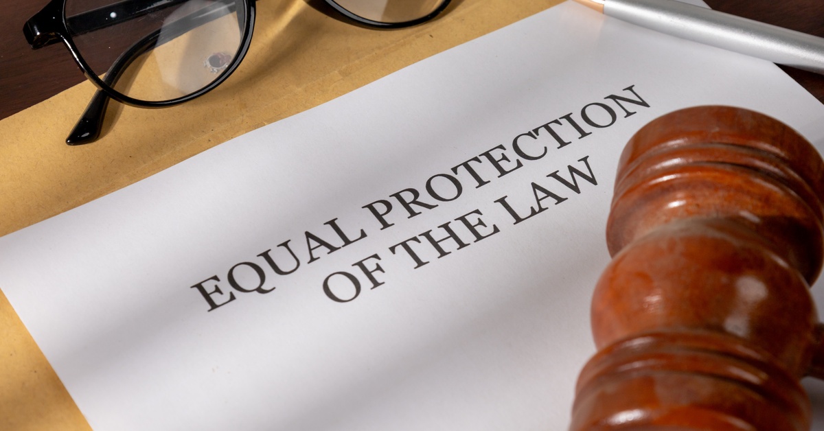 A brown gavel, silver pen, and eyeglasses sits on top of a document that says "Equal Protection of the Law".