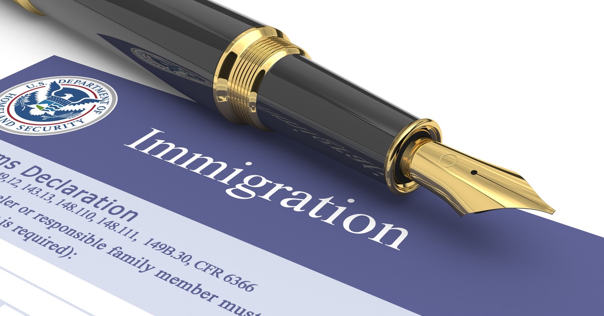 A black and gold fountain pen sits on top of a U.S. Immigration document sitting on top of a white table.