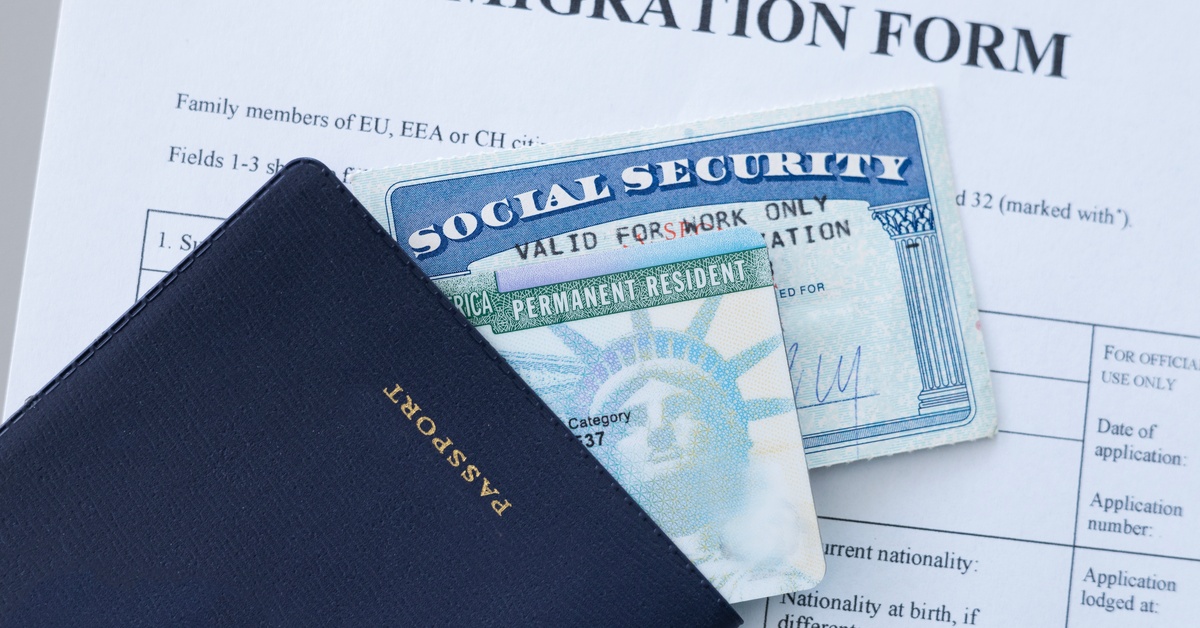 A passport with a social security card and permanent resident card inside, on top of immigration documents.