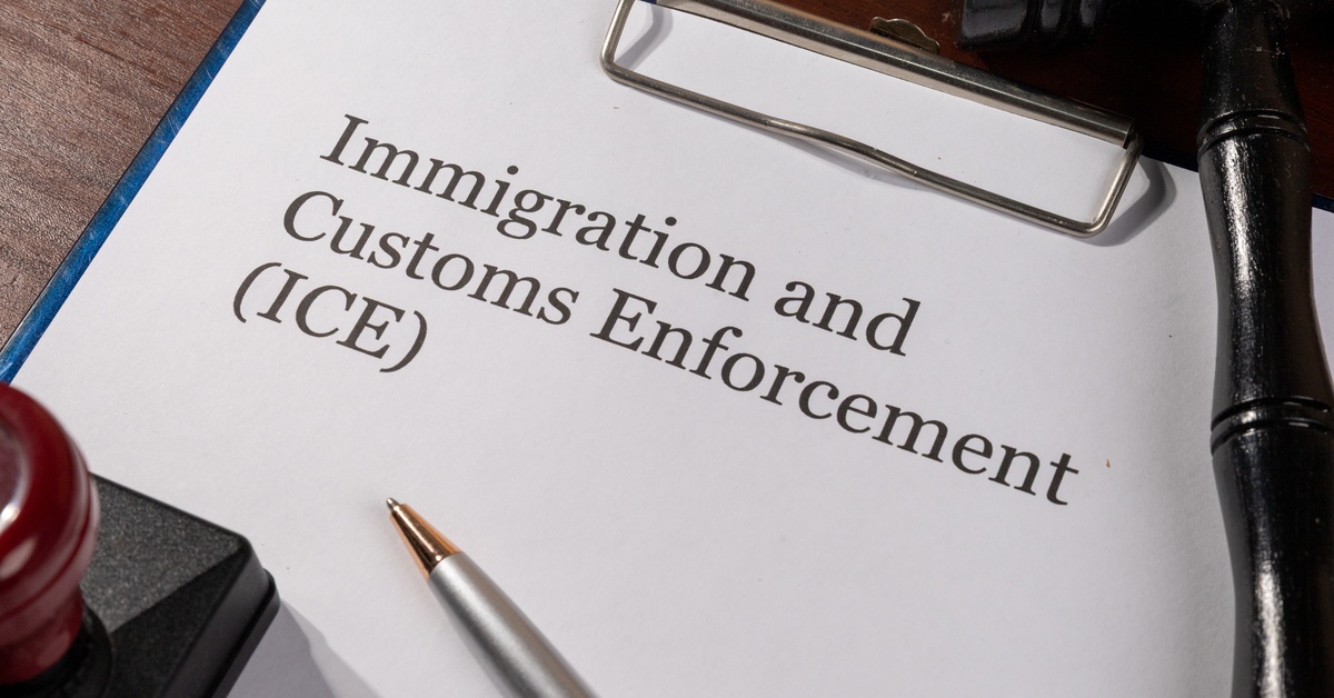 Printed “Immigration and Customs Enforcement (ICE)” document on a desk beside paperwork in an office setting.