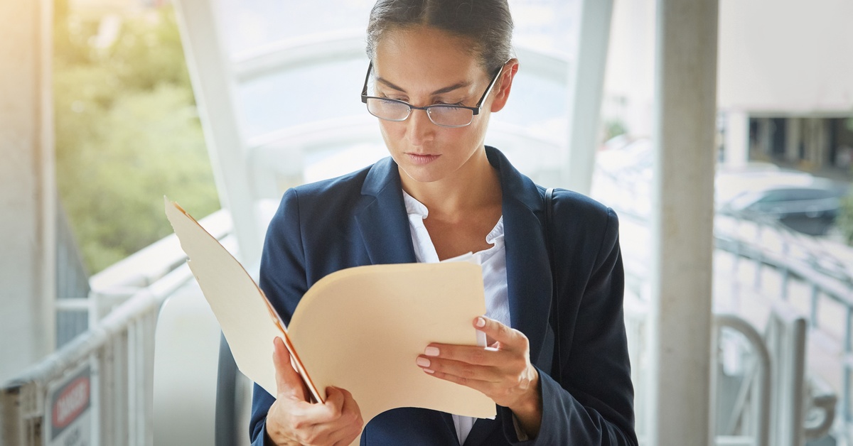 Woman commuting while reading documents and checklist, holding paperwork for a legal case schedule in transit.