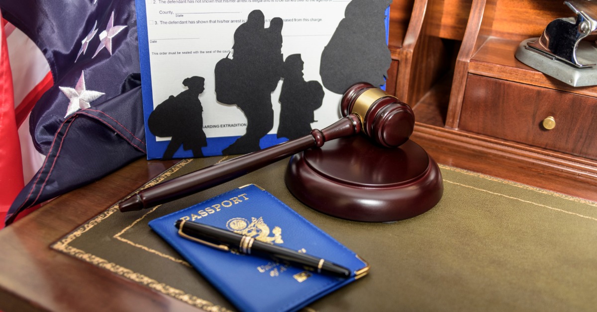 A gavel and passport on a wooden table with cardboard cutouts of people's silhouettes standing in front of a document.