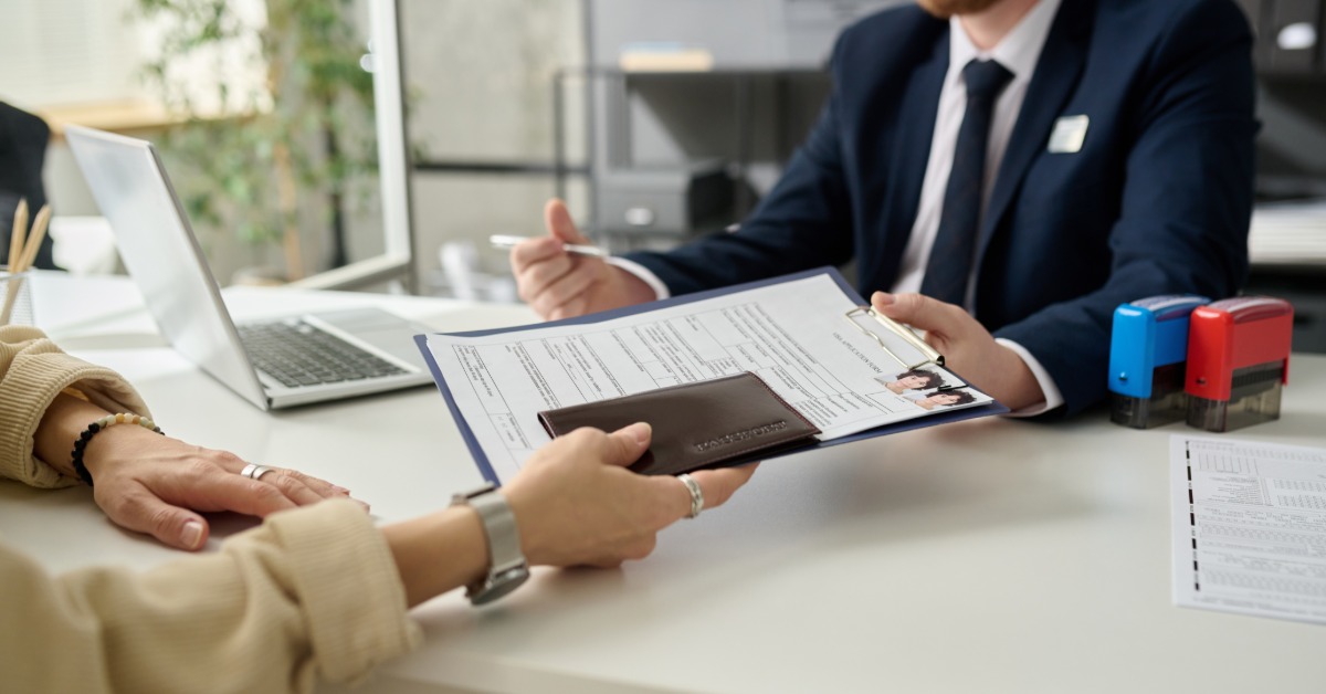 Close-up of a woman handing over immigration documents across a desk to an officer at a U.S. immigration office.