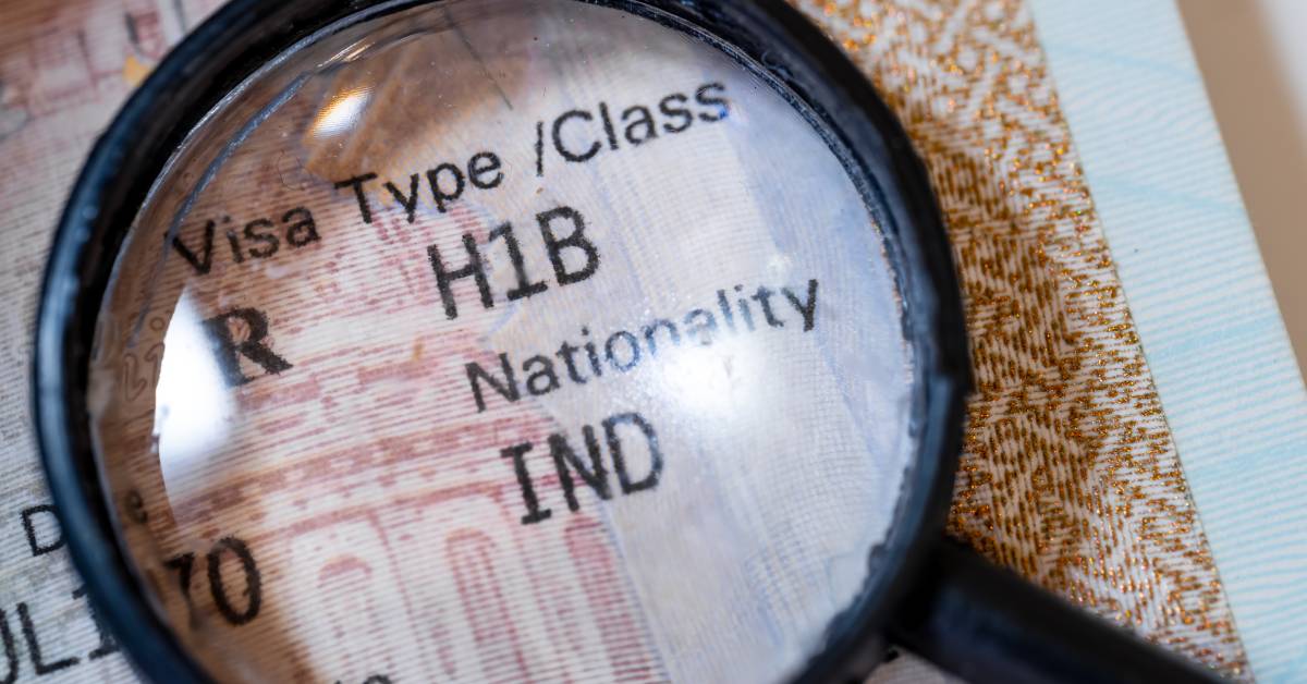 A magnifying glass placed on top of H-1B visa text with USA immigration details visible in the document.