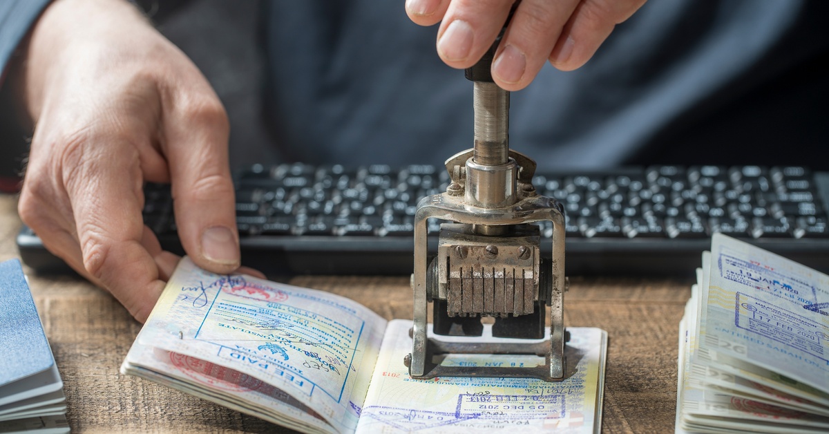 Close-up of a border control officer's hands stamping an international passport at an airport checkpoint.