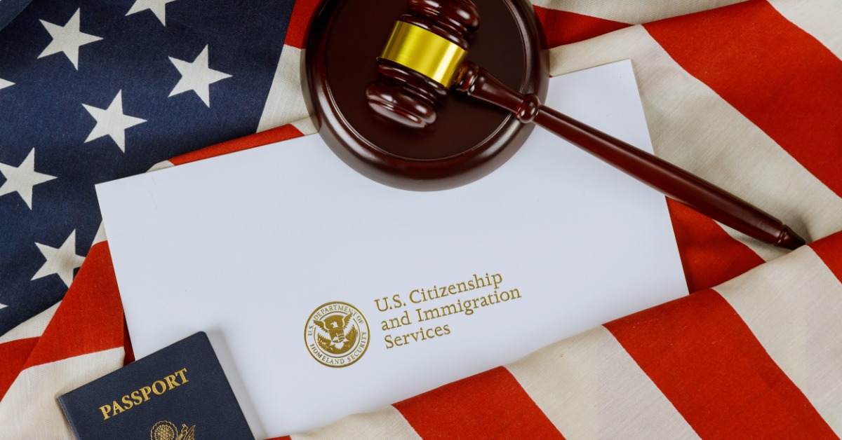 A wooden gavel resting on a white immigration services document with a passport on a folded United States flag.