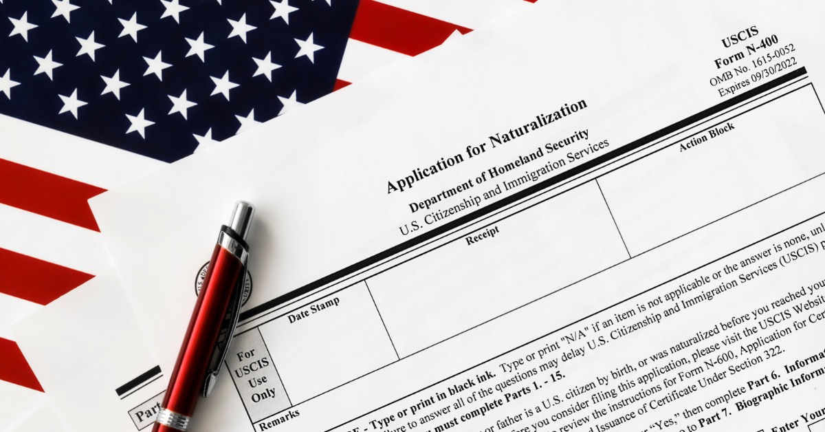 A red pen lying on an application for naturalization form placed across a folded United States flag.
