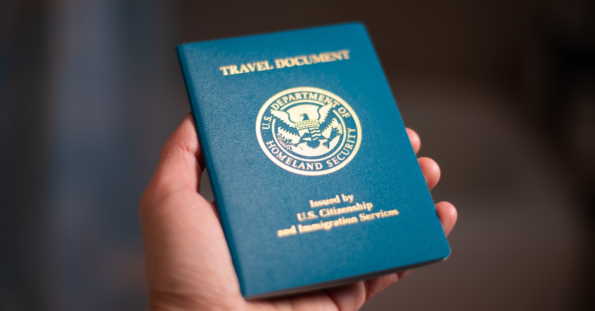 A person's hand is holding a travel document with the US Department of Homeland Security logo.