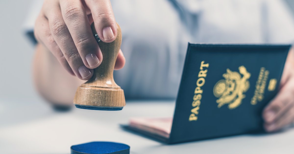A close-up of a person holding a stamp in one hand above a blue ink pad and a United States passport in their other hand.