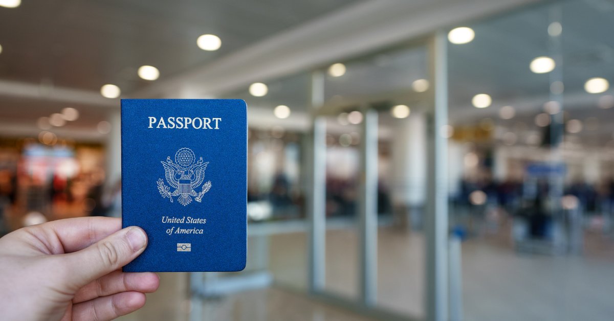 A close-up view of a person's hand holding a blue American passport with a blurred background of a building interior.