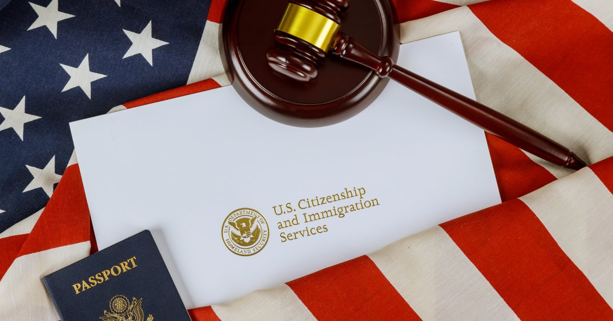 A paper that says "U.S. Citizenship and Immigration Services" sits next to a passport and gavel on top of the American Flag.