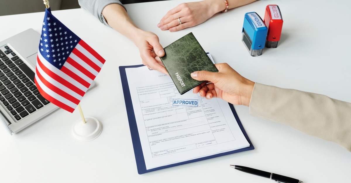 A bird's eye view of two people's hands holding a passport. On a table behind them is a document saying "approved."