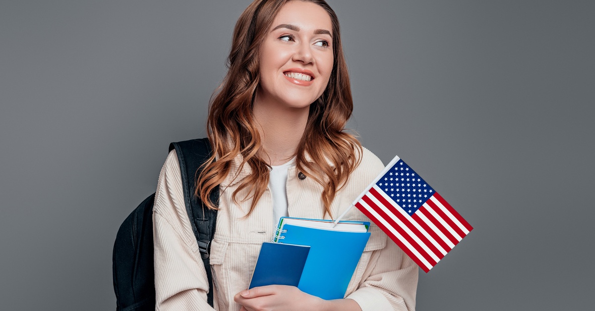 A woman holds a blue notebook with the United States Flag stuck in between while carrying a backpack.