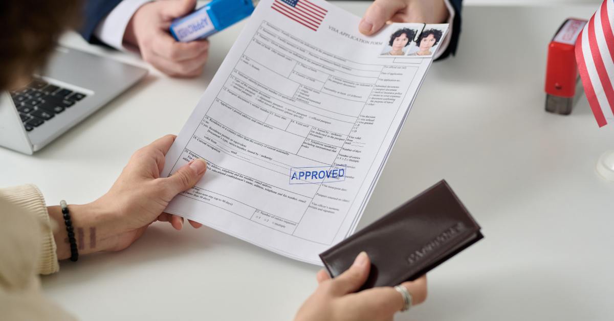 A person hands out visa application forms that are stamped with approved across the table to another person.