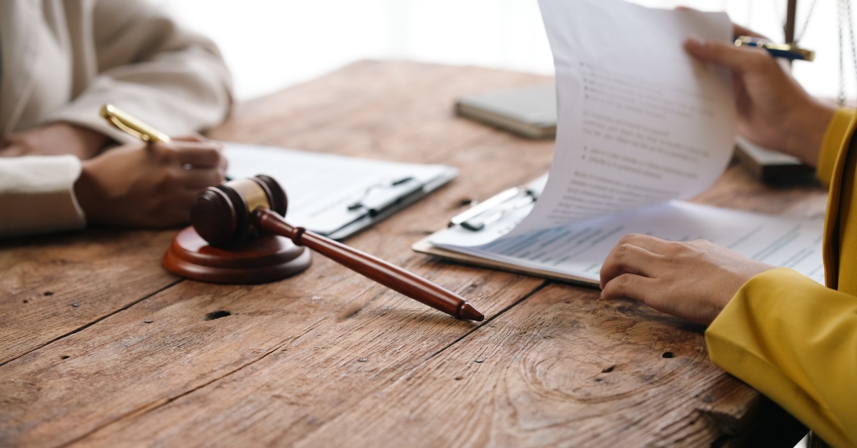 Two people sit across from each other on the wooden table while reviewing documents. On top of the table is a gavel.