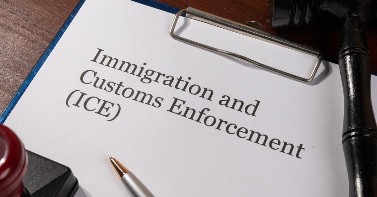 A clipboard with a document that says ICE sits on a wooden table next to a black gavel and a red stamp.