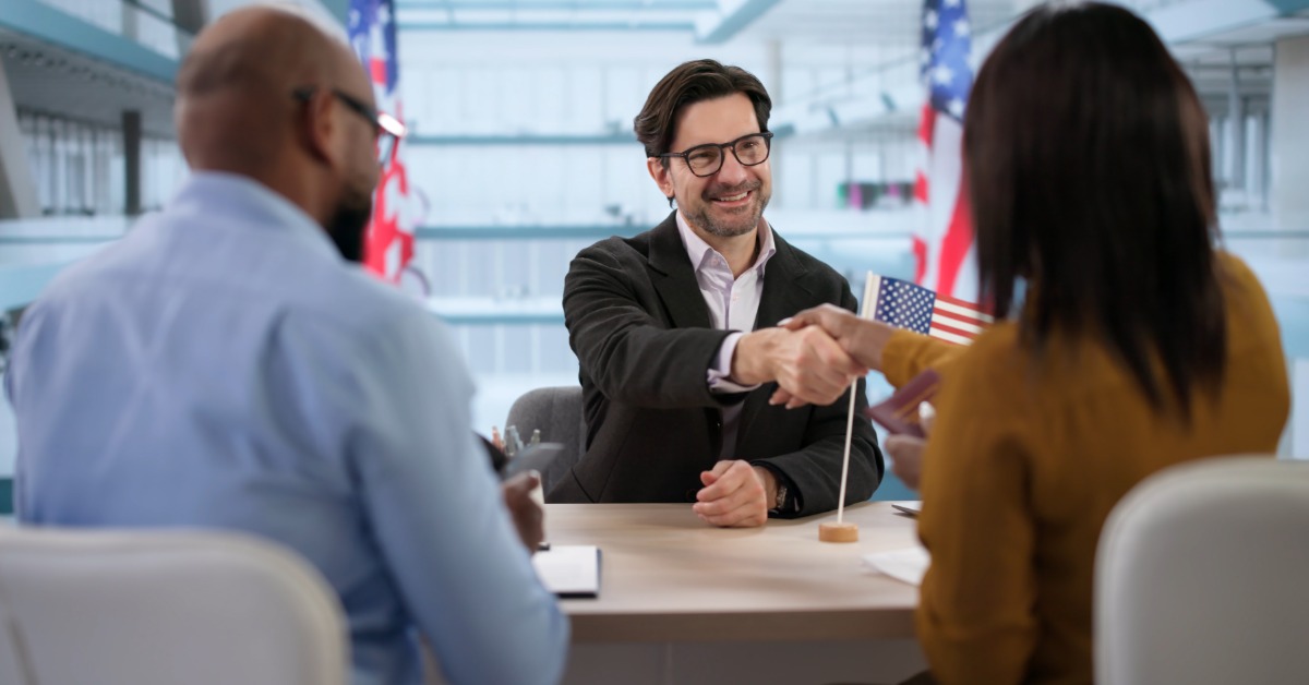 A smiling couple reviewing documents while an immigration lawyer assists them at a desk in an office.